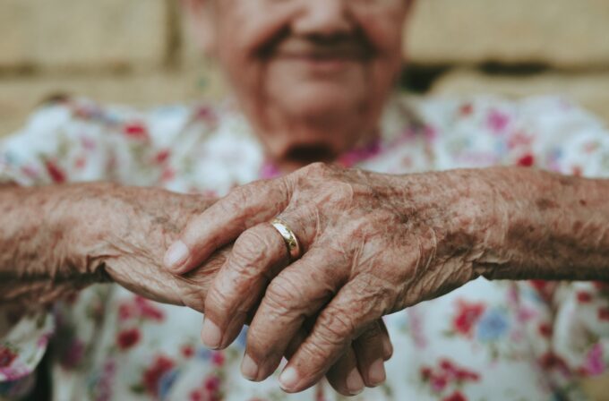 Anziana con le mani incrociate. In lontananza il volti