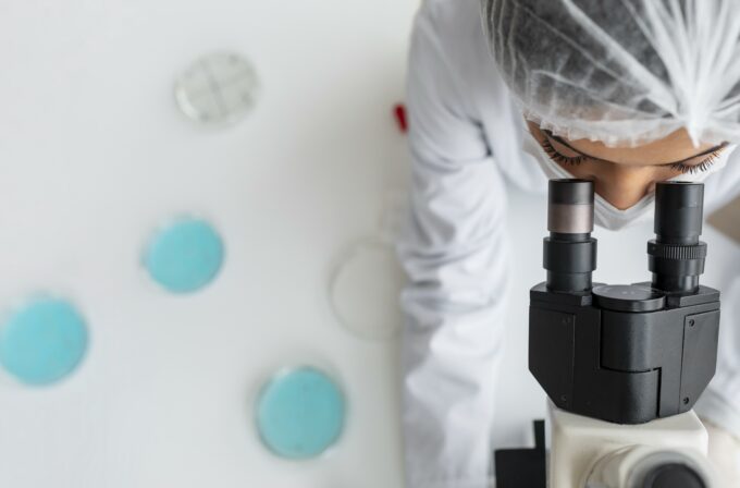 Scienziata che guarda un microscopio e studia la mutazione che protegge dall'Alzheimer